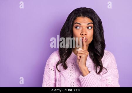 Photo of pretty tricky dark skin lady dressed knitted pullover finger lips looking empty space isolated purple color background Stock Photo