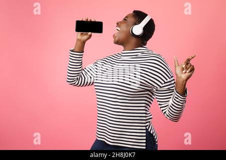 Black Woman Singing Holding Smartphone Like Microphone Over Pink Background Stock Photo