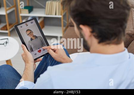 Man on digital tablet looks at profile photo of attractive young woman in dating app. Stock Photo