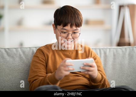 Joyful korean teenager playing games on cellphone Stock Photo