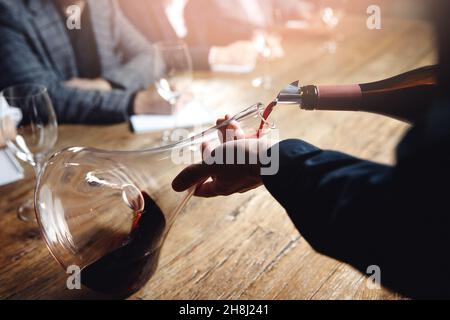 Sommelier and bartender training, Closeup hand of man pouring red wine from bottle into decanter. Stock Photo
