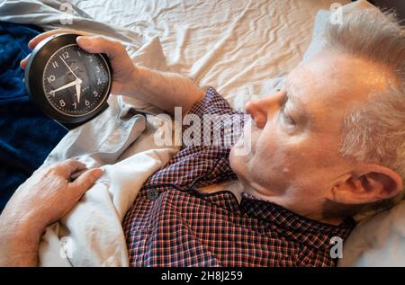 Mature man Sleepless, Tossing and Turning, Looking at Clock Stock Photo