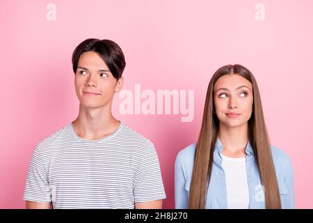 Photo of adorable doubtful young couple wear casual clothes looking empty space smiling isolated pink color background Stock Photo