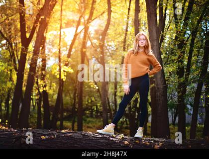 Tween girl with Red Hair standing on a log in the woods. Stock Photo
