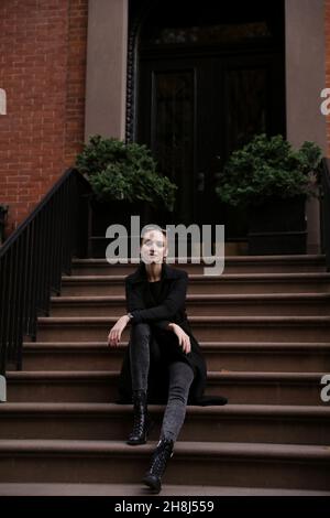 Young woman in black coat sits on the steps of the house Stock Photo