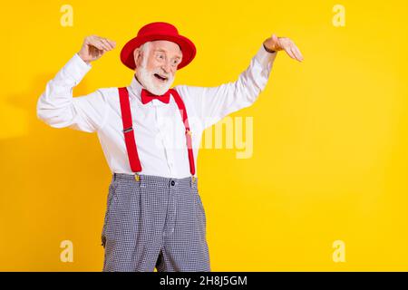 Photo of lovely elder man dance look ad wear red cap tie shirt suspenders trouseres isolated on yellow background Stock Photo