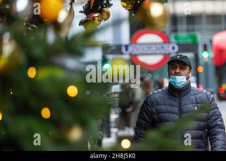 London, UK.  30 November 2021.  A man passes Christmas trees outside Harvey Nichols in Knightsbridge on the first day that face coverings are again required in shops following the UK government’s new measures to try to curb the spread of coronavirus following the detection of the Omicron variant.  Credit: Stephen Chung / Alamy Live News Stock Photo