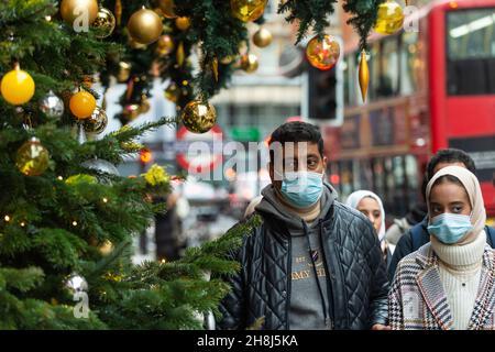 London, UK.  30 November 2021.  A couple passes Christmas trees outside Harvey Nichols in Knightsbridge on the first day that face coverings are again required in shops following the UK government’s new measures to try to curb the spread of coronavirus following the detection of the Omicron variant.  Credit: Stephen Chung / Alamy Live News Stock Photo