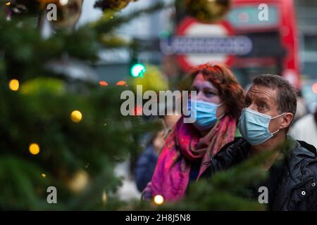 London, UK.  30 November 2021.  A couple passes Christmas trees outside Harvey Nichols in Knightsbridge on the first day that face coverings are again required in shops following the UK government’s new measures to try to curb the spread of coronavirus following the detection of the Omicron variant.  Credit: Stephen Chung / Alamy Live News Stock Photo