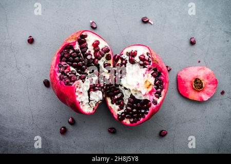 Seeding a Pomegranate on a Dark Background: A split pomegranate being seeded on a concrete countertop Stock Photo