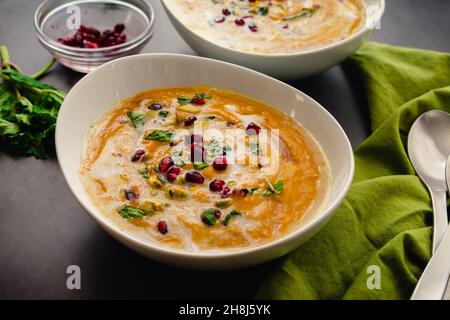 Bowls of Moroccan Roasted Pumpkin Soup: Roasted pumpkin soup garnished with mint leaves, pomegranate seeds, and chopped pistachios Stock Photo