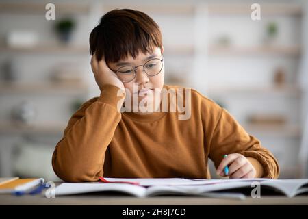 Bored schooler doing homework, leaning on his hand Stock Photo