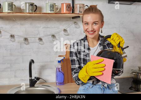 Domestic service and housekeeping concept, happy blonde lady cleaning kitchen kettle. Stock Photo