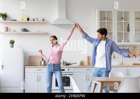 Happy cheerful millennial husbands lady dancing, have fun together in kitchen interior Stock Photo