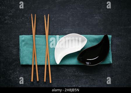 Black and white ceramic bowls and chopsticks lying on linen napkin, dark background, top view Stock Photo