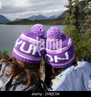 People wearing Yukon bobble hats, known as toquesin the Yukon, Canada. They look outonto one of the territory's lakes. Stock Photo