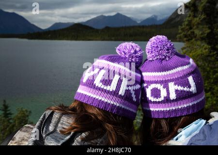 People wearing Yukon bobble hats, known as toquesin the Yukon, Canada. They look outonto one of the territory's lakes. Stock Photo