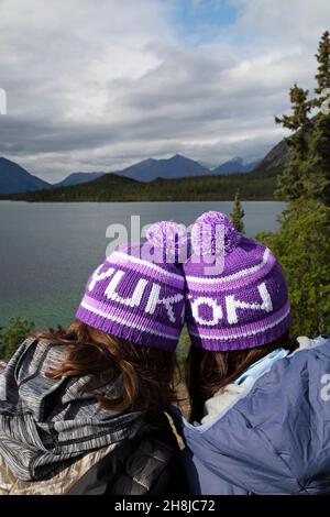 People wearing Yukon bobble hats, known as toquesin the Yukon, Canada. They look outonto one of the territory's lakes. Stock Photo