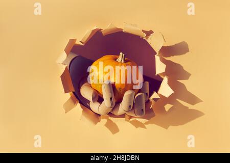 Orange pumpkin in wooden model hand through paper hole in torn beige paper. Hello Autumn season Stock Photo