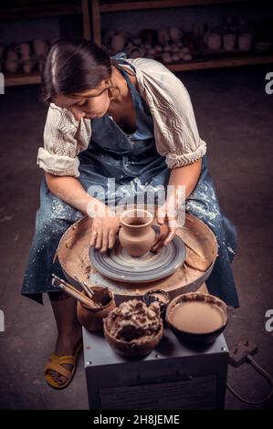Stylish handicraftsman master making pottery, sculptor from wet clay on wheel. Artisan production. Stock Photo