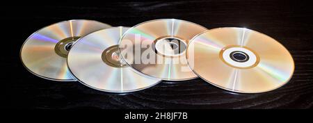 Four blank CD discs spread out and isolated on a black table with selective focus. Stock Photo