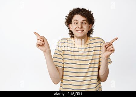 Excited smiling young man pointing left and right, showing two ways, demonstrating variants, white background Stock Photo