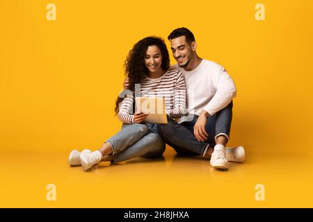 Cheerful Young Arab Couple Browsing Internet On Digital Tablet In Studio Stock Photo