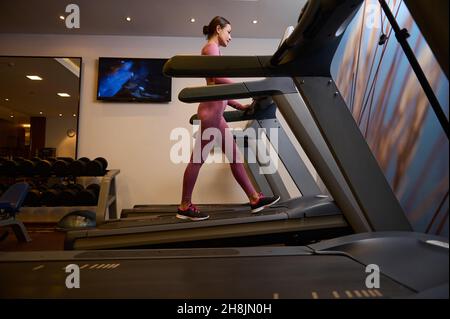 Side view of a middle aged European woman in sportswear exercising on a treadmill at gym. Cardio workout. Stock Photo