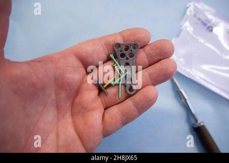 an explanted titanium plate and various titanium screws of a radius fracture are in one hand Stock Photo