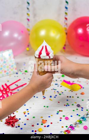 Mom's hand passes an ice cream cone to the child's hand on a birthday background with colorful decor and sweets with blurred background. Selective Stock Photo