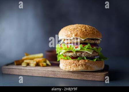 delicious large double burgeon with vegetables cutlet veal meat with lettuce and cheese on a wooden board .Hamburger with fries Stock Photo