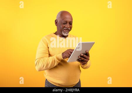 Positive elderly black man using digital tablet for freelancing job or studies on orange studio background Stock Photo