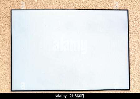 White blank advertising sign with black frame hanging outside at the exterior wall of a building Stock Photo