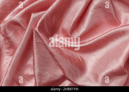 Folded shiny wrinkled satin of pale coral pink color texture. Background of draped powder pink silk cloth. Elegant luxury silky crumpled material. Stock Photo