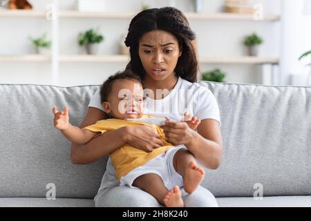 High Fever. Concerned Black Mom Checking Temperature Of Her Crying Infant Baby Stock Photo