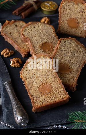 Sliced Christmas muffin with hazelnuts and salted caramel, covered with chocolate icing on a slate board on dark background Stock Photo