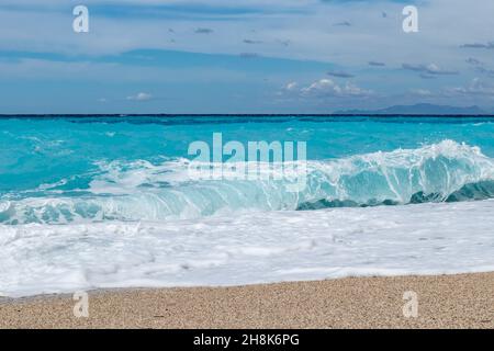 Azure vibrant breaker waves hitting shore. Sunny coast of Greek island with blue sky. Sandy beach in Greece. Summer nature travel to Ionian Sea Stock Photo