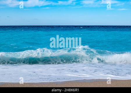 Azure vibrant breaker waves hitting shore of Greek island with blue sky. Sandy beach in Greece. Summer nature travel to Ionian Sea Stock Photo