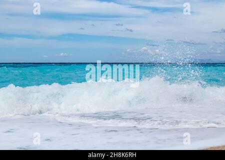 Azure breaker waves with white foam hitting shore. Coast of Greek island with blue sky. Sandy beach in Greece. Summer nature travel to Ionian Sea Stock Photo