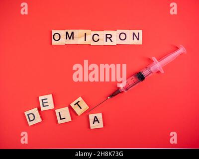 Omicron variant replaces Delta. Emergence of new dangerous strain of coronavirus COVID-19 Omicron. Syringe. Words omicron delta on colored red backgro Stock Photo