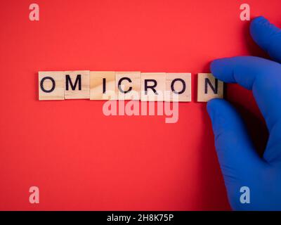 Omicron variant replaces Delta. Emergence of new dangerous strain of coronavirus COVID-19 Omicron. Blue gloves on hand. Words omicron on colored red b Stock Photo
