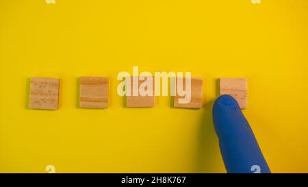 Hand in blue gloves point on clean wooden blocks on colored yellow background. Medical scientific or biological theme. Template for text or concept. A Stock Photo