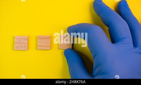 Hand in blue gloves point on clean wooden blocks on colored yellow background. Medical scientific or biological theme. Template for text or concept. A Stock Photo