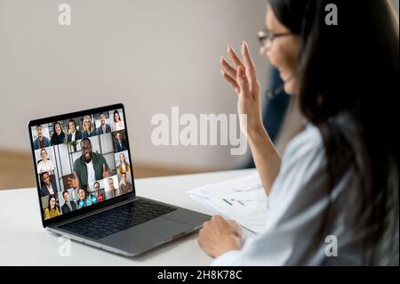 Virtual meeting, brainstorm of colleagues, online conversation. Over shoulder woman view to a computer screen, talks on video call with multiracial business group, discussing the project, greeting Stock Photo
