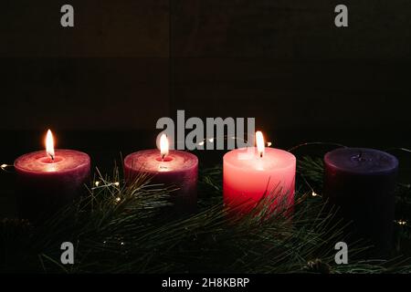 Three pillar candles lit on an advent wreath in a dark room for the fourth week of advent with copy space Stock Photo
