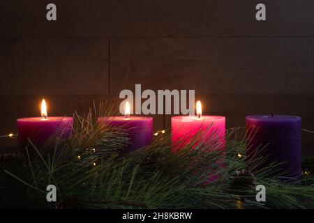 Three pillar candles lit on an advent wreath in a dark room for the fourth week of advent with copy space Stock Photo