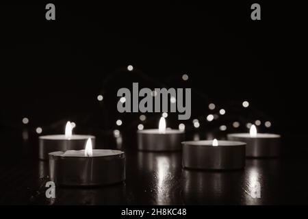 Mini tea light candles burning in the dark with fairy lights and flame reflecting off of dark wood table with copy space Stock Photo