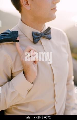 Groom in a beige shirt and bow tie holds his jacket on his shoulder with his finger. Close-up Stock Photo