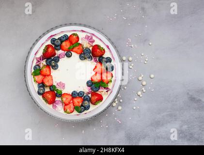Delicate cake garnished with fresh strawberries blueberries on a gray plain background. Festive dessert with berries Stock Photo