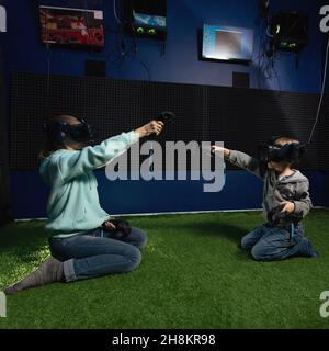 amazed children using virtual reality headsets and controllers build and draw in front of them while sitting on floor. Futuristic gadget concept Stock Photo